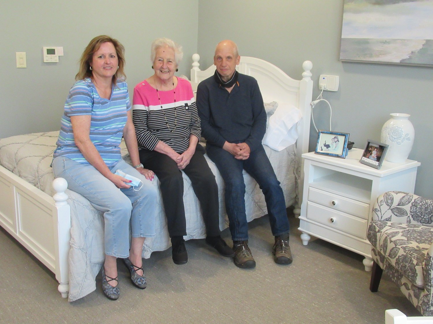 FANTASTIC FIRST: Madeleine Brantley (center), 93, sits on her new bed inside The Preserve with her daughter Pamela Miller and son-in-law David Miller. Brantley was the first female resident to move into the Johnston facility.